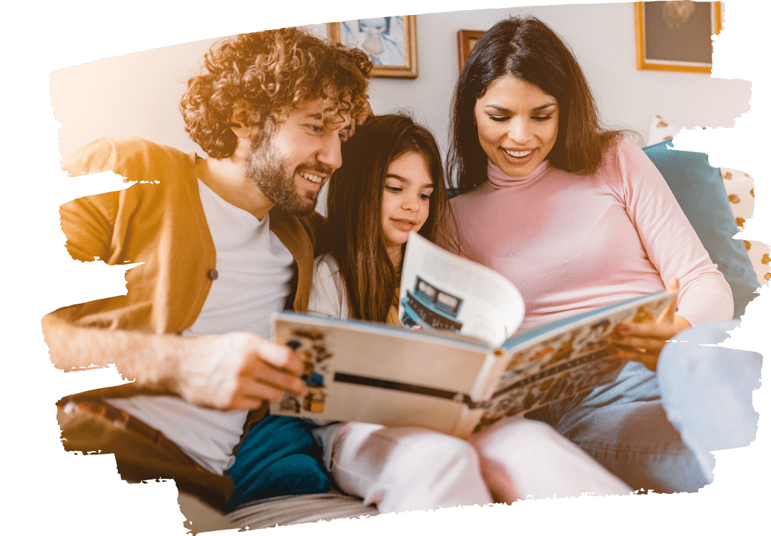 A child sitting between two parents on a couch reading a book together