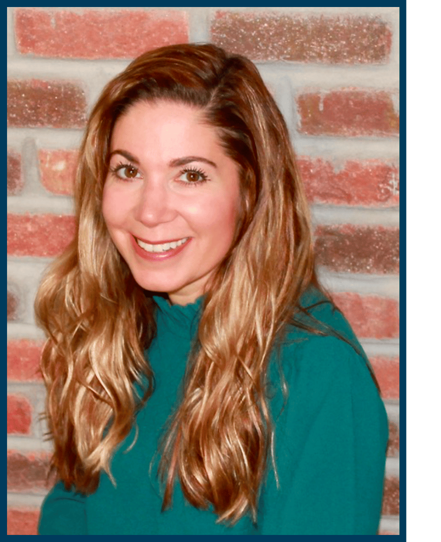 Brown-haired, brown-eyed woman wearing teal turtle-neck top smiling in front of brick background